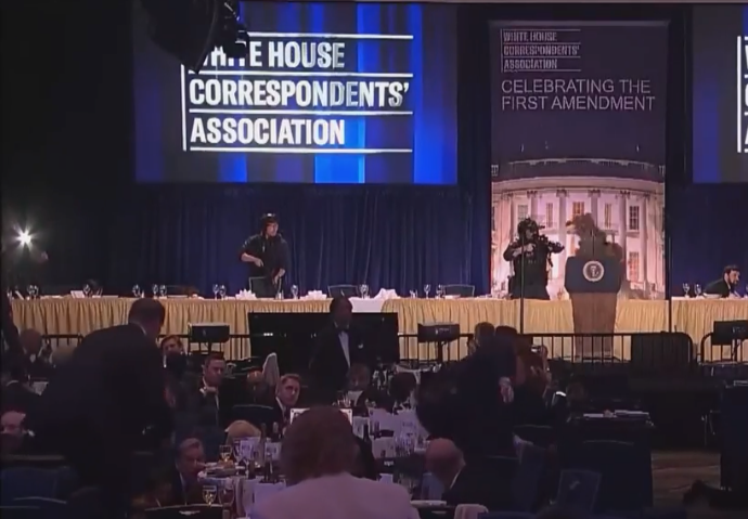 Sala balowa z napisem White House Correspondents Association, na scenie mównica prezydencka, uczestnicy siedzą przy stołach