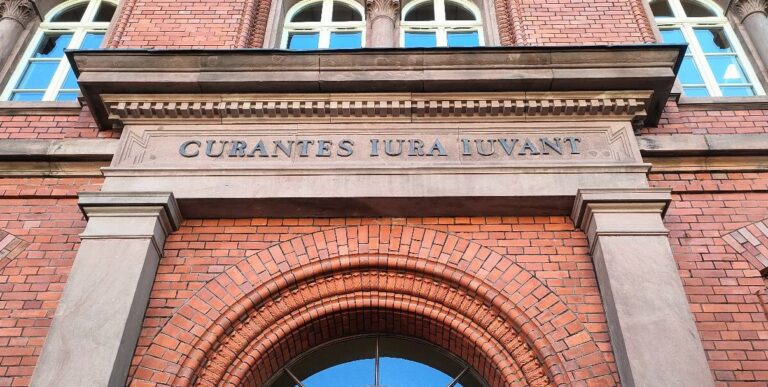 Napis Curantes Iura Luvant nad łukowym wejściem do budynku sądu z czerwonej cegły