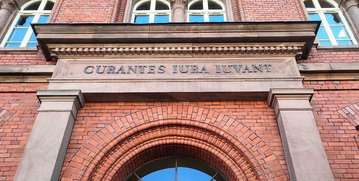 Napis Curantes Iura Luvant nad łukowym wejściem do budynku sądu z czerwonej cegły