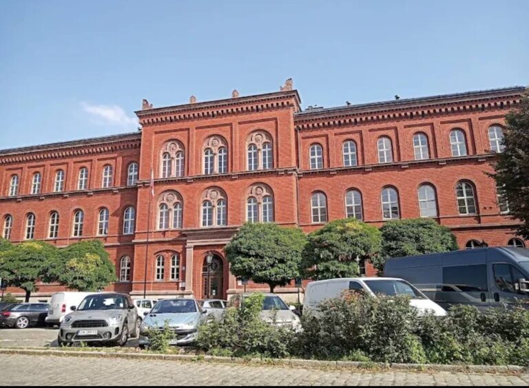 Zabytkowy czerwony ceglany budynek Sądu Okręgowego w Świdnicy z charakterystycznymi łukowymi oknami i parkingiem przed wejściem