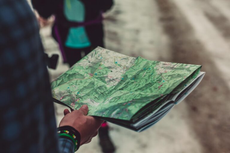 Osoba trzymająca topograficzną mapę turystyczną z zaznaczonymi szlakami i punktami podczas wędrówki górskiej