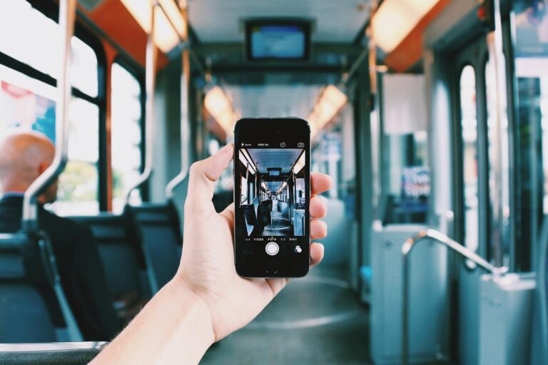 Ręka trzymająca smartfon z włączoną aplikacją aparatu fotografującą wnętrze tramwaju, symbolizująca użytkowanie urządzeń mobilnych
